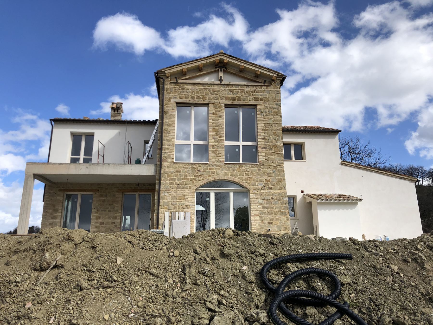 Fronte a valle di un casale in fase di finitura, con paramento in pietra e grandi aperture