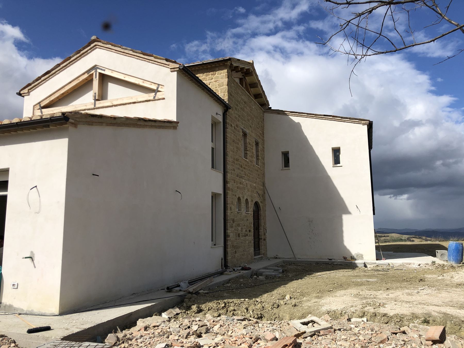 Vista di spigolo di un casale con intonaco bianco fresco e volume in pietra, macerie di cantiere a terra