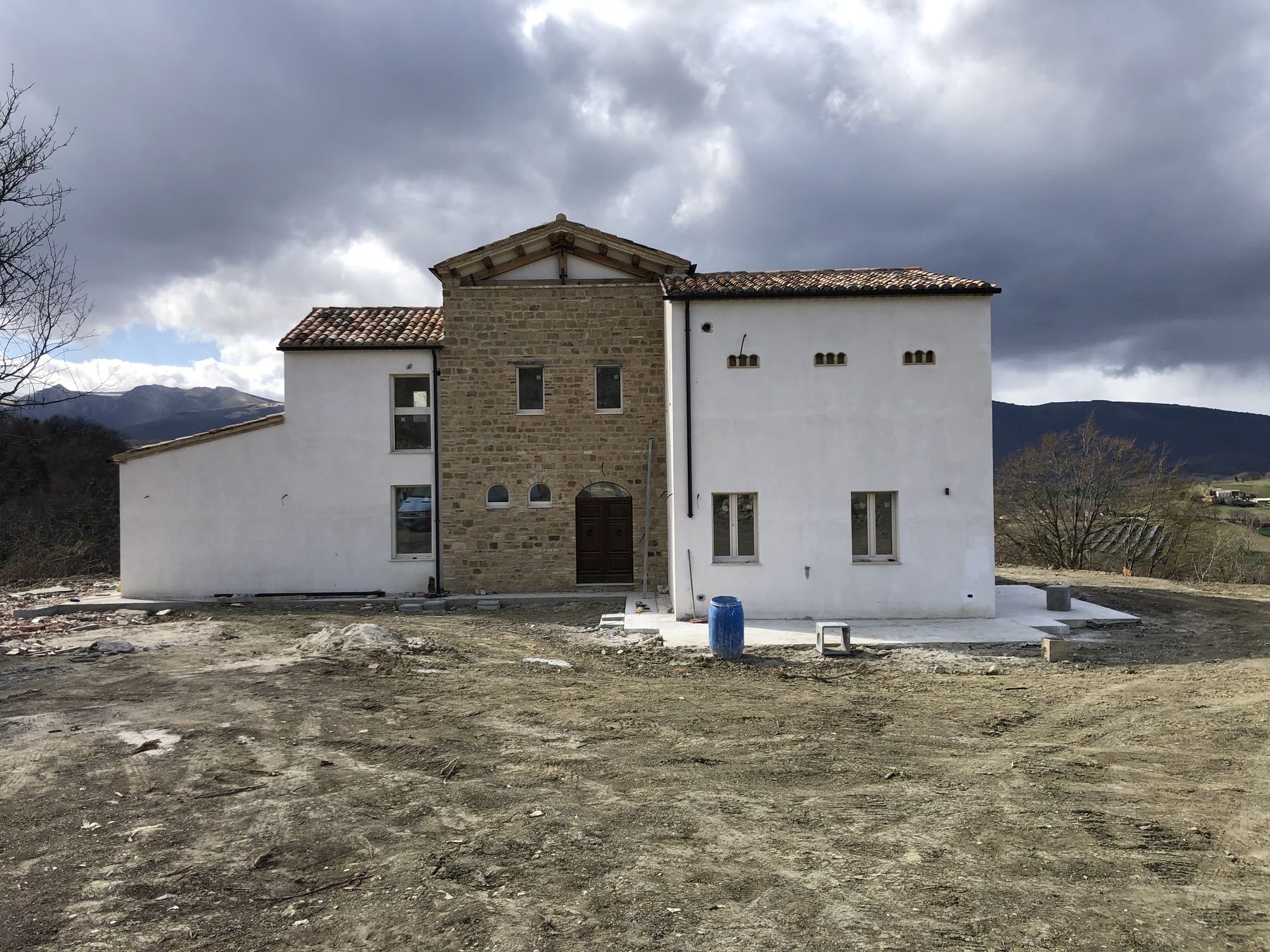 Edificio di nuova costruzione con corpo centrale in pietra squadrata e ali intonacate, montagne sullo sfondo
