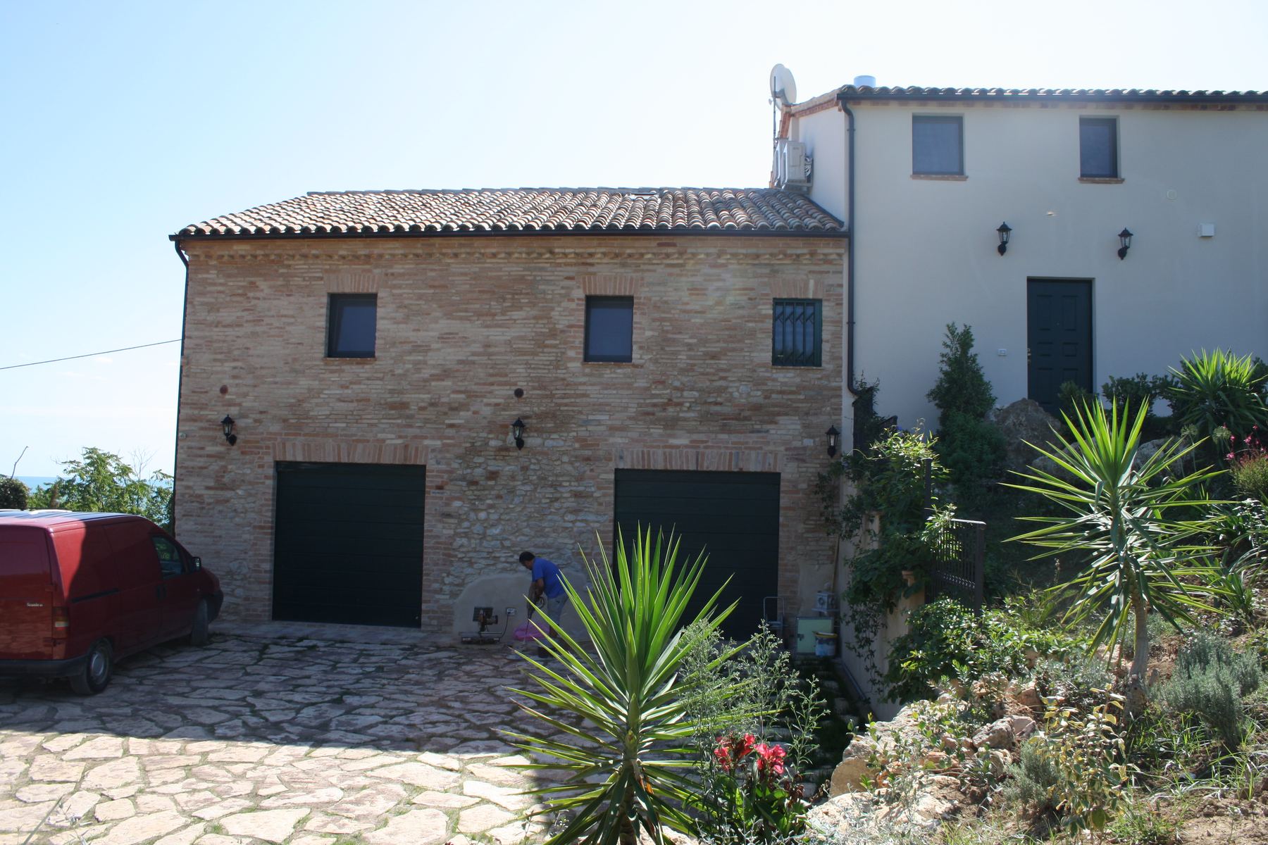 Corte con pavimentazione in lastre di pietra, edificio in mattoni con due portoni e piante grasse