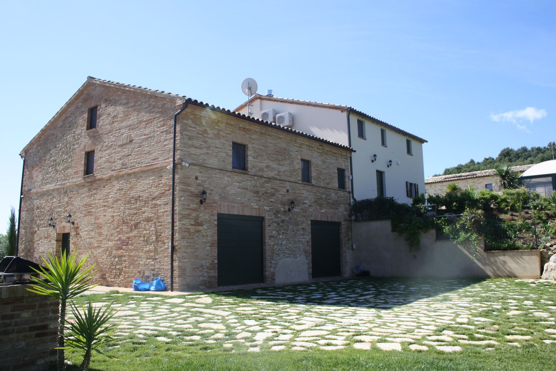 Grande fienile in laterizio con due portoni scuri e corte pavimentata a lastre di pietra su prato