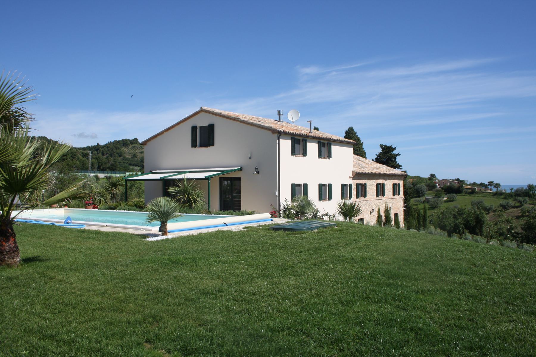 Casale bianco con nuovo volume e pergolato, piscina lunga sul prato in pendenza