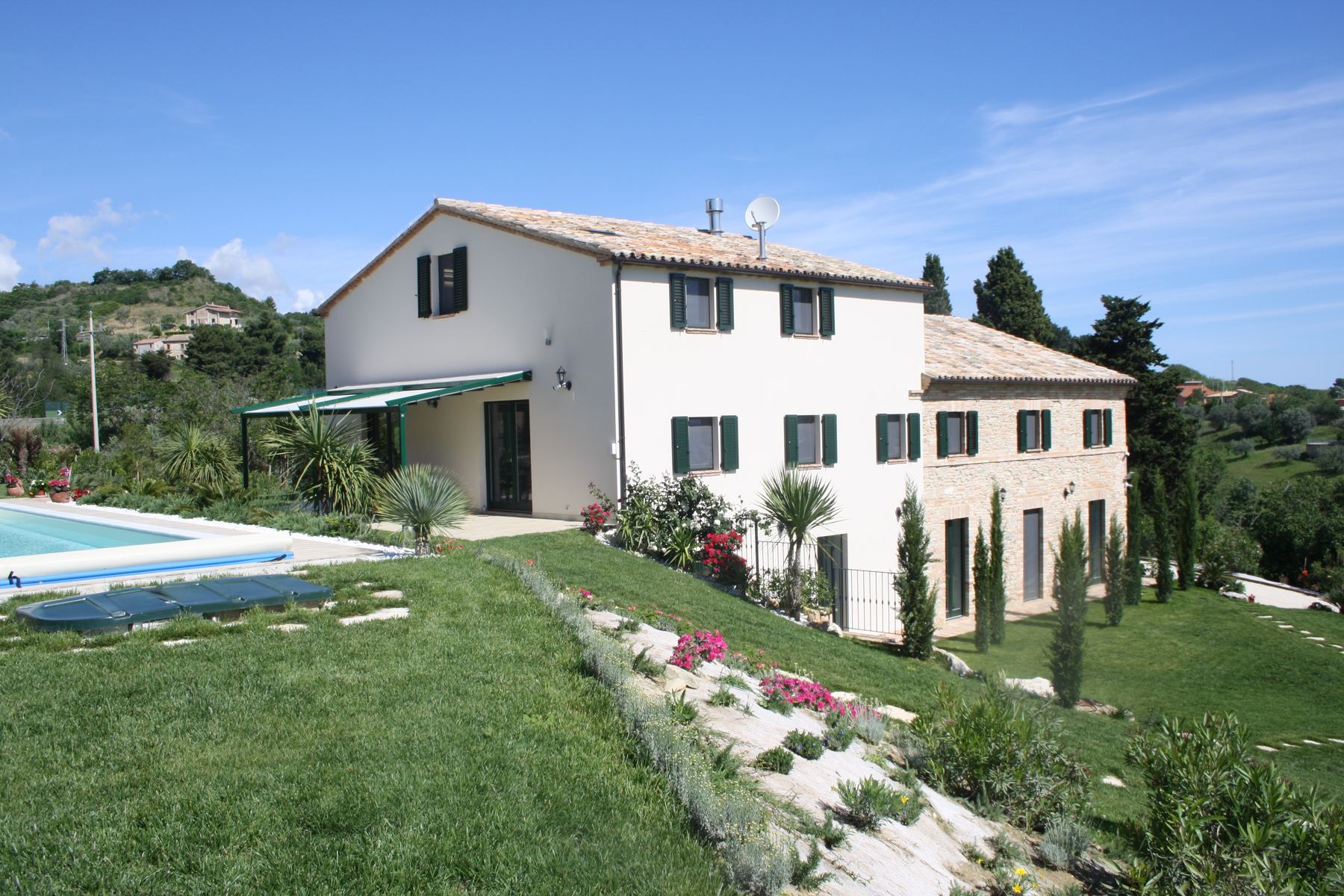 Casale intonacato a calce con ala in pietra a vista, persiane verdi, piscina e scarpata fiorita