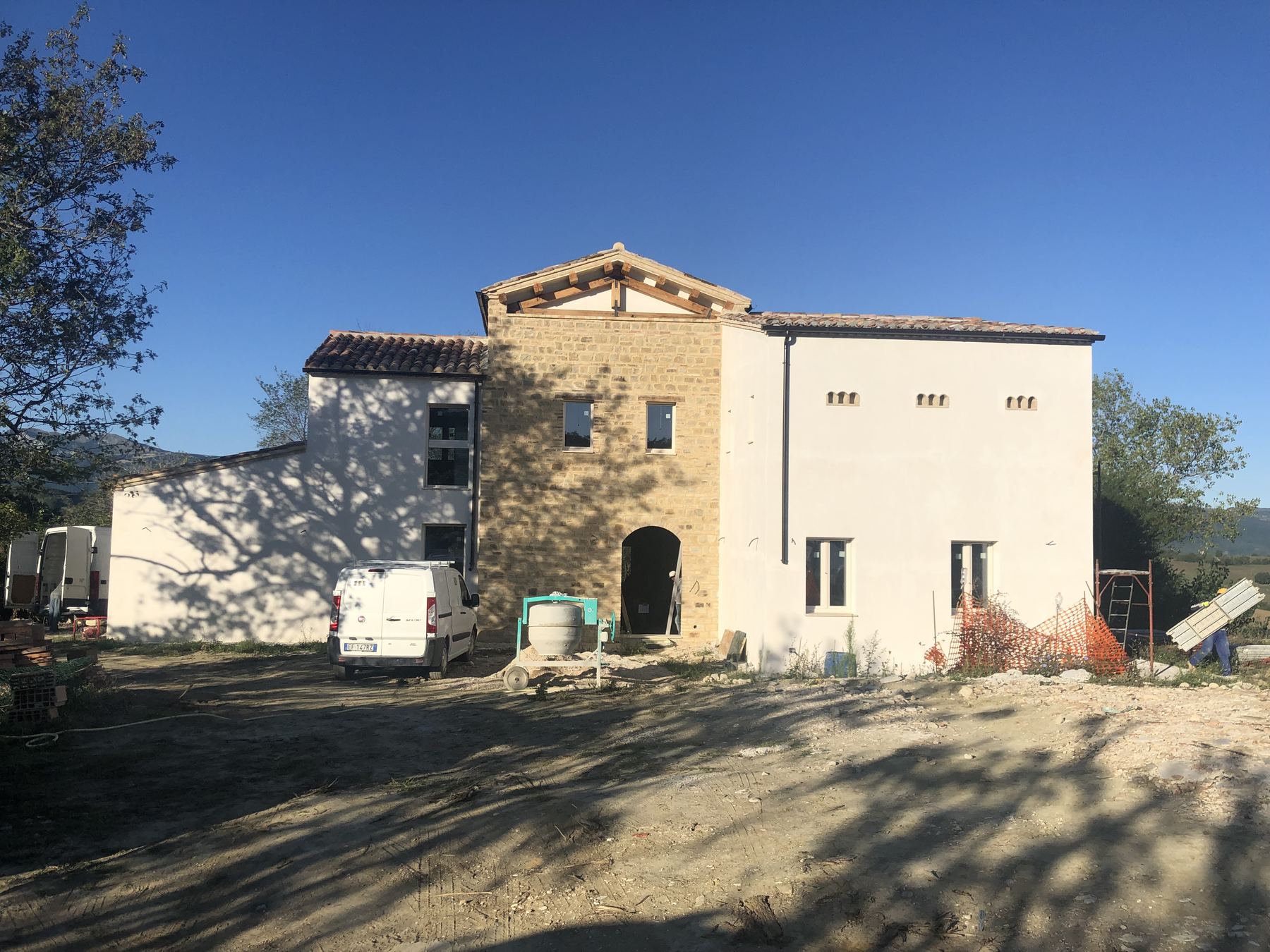 Casale con intonaci bianchi appena ultimati e torre in pietra, mezzi di cantiere nel piazzale
