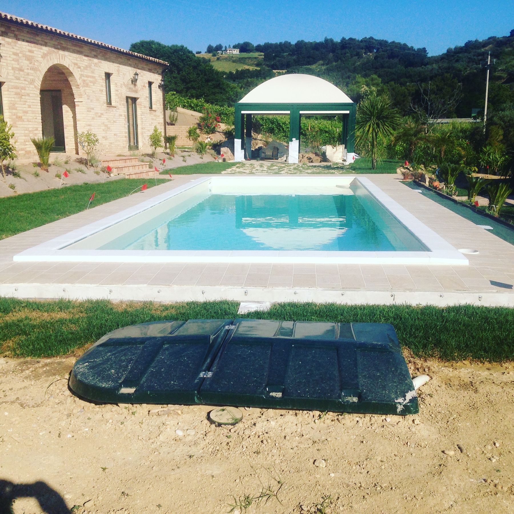 Piscina rettangolare con bordo chiaro, gazebo verde e vano tecnico interrato in primo piano